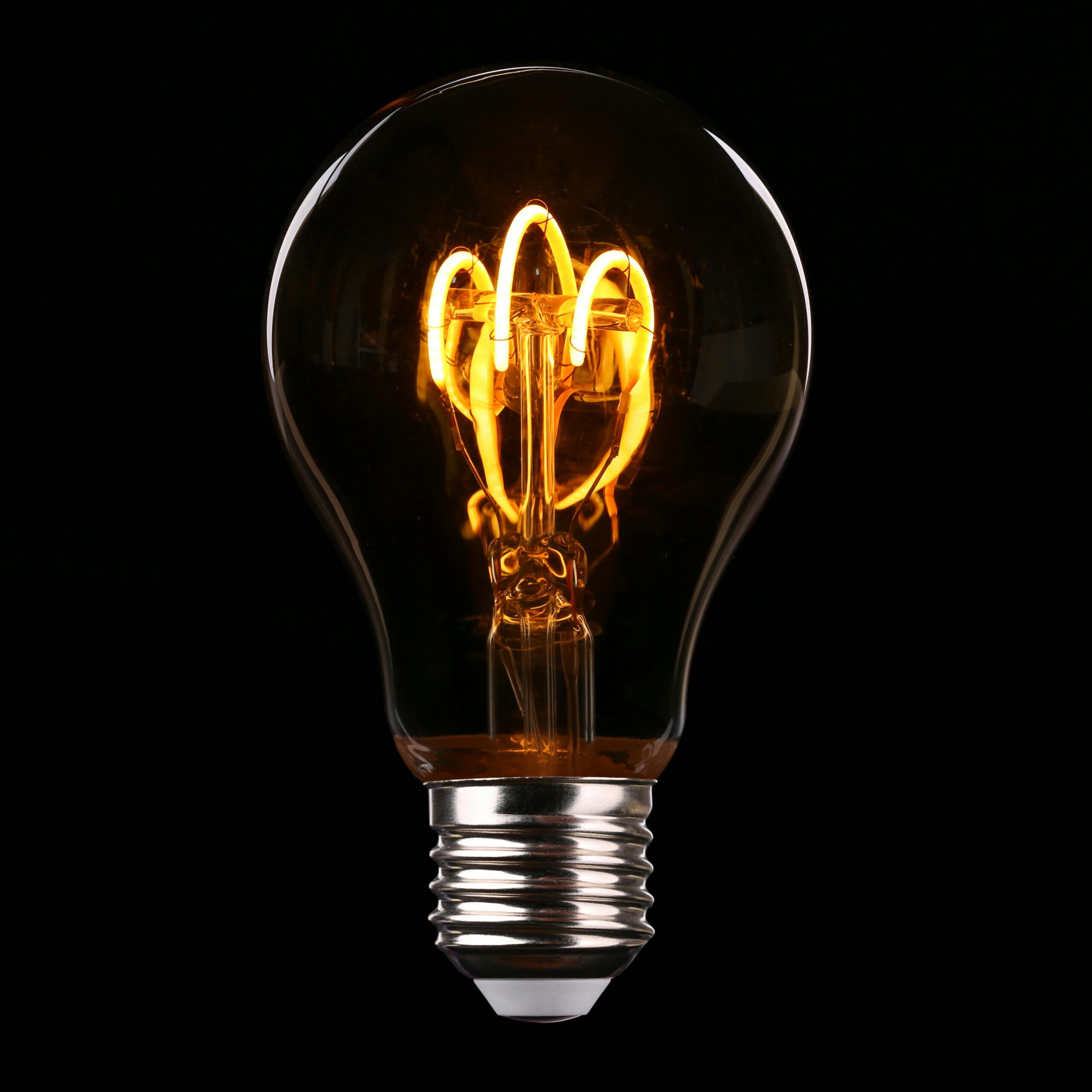 Close-up of an illuminated Edison-style light bulb on a dark background.